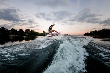 view on active athletic woman jumping over splashing wave on surf style wakeboard.