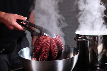 Boiled octopus is taken out of the pan. The whole carcass of an octopus. Pot of hot water in the...