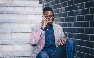 Young African American man having cheerful conversation on his mobile phone, sitting on stairway of building