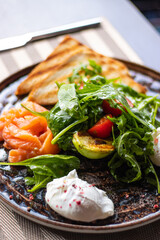 Healthy breakfast with smoked  salmon, greens, tomatoes, poached egg, avocado, salad and toasts. 