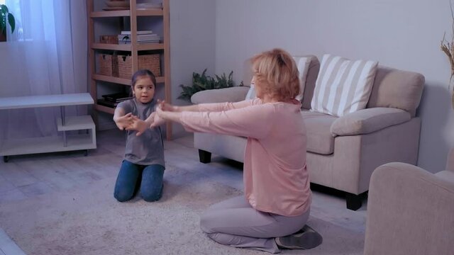 Grandmother and her granddaughter making physical jerks in the room. Indoors activities. Healthy lifestyle. Good habits. Woman and child . High quality 4k footage
