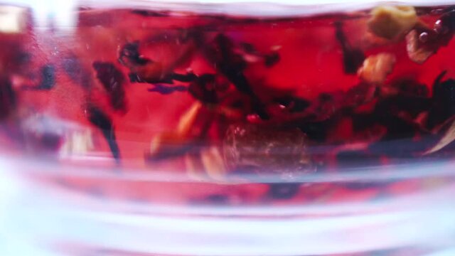 Brewing red tea with boiling water. Adding water to tea leaves with currants, flowers. Making tea in a glass teapot. Tea ceremony. Close-up