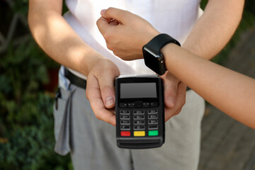 Woman using smartwatch for contactless payment outdoors, closeup