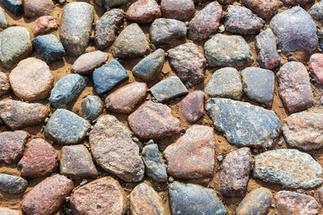 Rounded pebble stones background. Natural large sea cobblestones wallpaper with different size and color gray texture. Sunny day light on rocks in the sand. Top close up view photo with copy space.