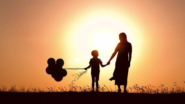 Silhouette of a happy family at sunset. A mother and a child with balloons hold each other's hands. Beautiful orange background