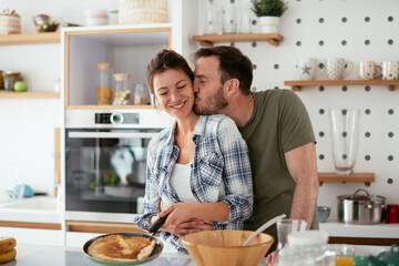 Young couple making pancakes at home. Loving couple having fun while cooking.