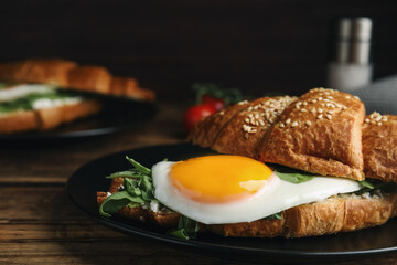 Delicious croissant with arugula and fried egg on wooden table, closeup