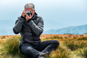 Fototapeta premium Photographer with old analog camera at a Mountain top. Mountain landscape view. Mountain layers landscape. Meadows and mountains landscape. Blue mountains layers landscape. Top of the Mountains