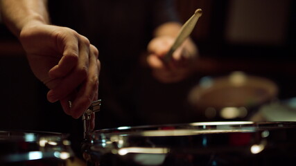 Unrecognizable musician tuning drum kit in studio. Drummer hitting drum in hall.