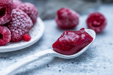 Closeup shot of raspberry jam with frozen raspberries in the background