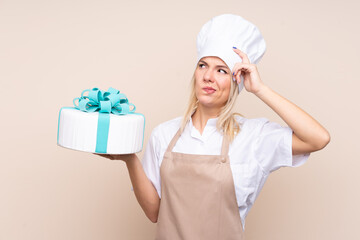 Young Russian woman with a big cake over isolated background having doubts and with confuse face expression