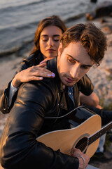Fototapeta na wymiar Selective focus of man playing acoustic guitar near woman on beach near sea at sunset