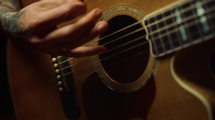 Unrecognizable person playing acoustic guitar in dark recording studio.