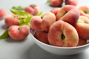 Fresh ripe donut peaches in bowl on light table, closeup