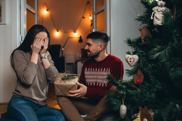 man gives christmas gift to his girlfriend, sitting at home