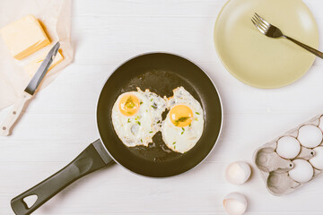 Fried eggs in frying pan next to empty plate with fork