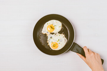 Woman's hand holding frying pan with delicious fried eggs