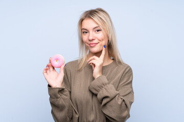 Young blonde woman over isolated blue background holding a donut