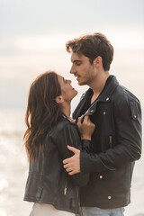 Young woman touching leather jacket of boyfriend near sea