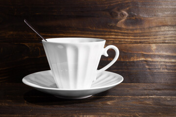 White porcelain cup and saucer with spoon on brown wooden surface