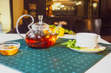 Aromatic hot green tea in a glass teapot with a warm blurry background with honey and fresh mint leaves. Served table with tea in a cafe