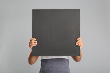 Man holding black blank poster on grey background. Mockup for design