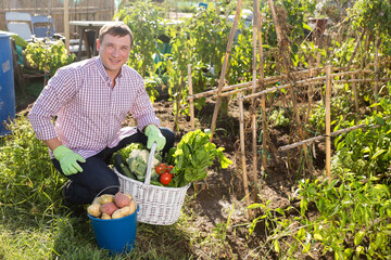 Young man gardener holding basket with harvest of vegetables in garden outdoor