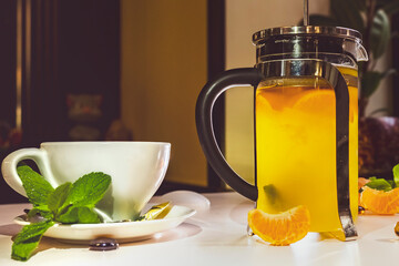 cup of hot tea and a teapot, mendarines, mint, honey. Tangerine tea on white table in restaurant