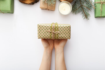 Female hands hold a box with a Christmas gift on white table with Christmas decorations. Christmas, Xmas, winter, new year, zero waste concept. Flat lay, top view, copy space, background.