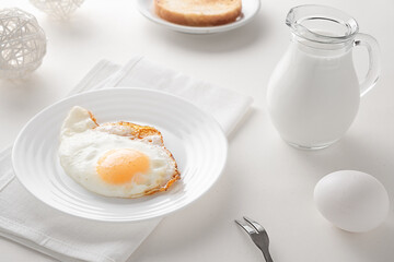 Breakfast fried eggs and a decanter of milk in a high key on a white table