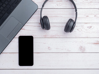 Top view of headphones, smartphone and laptop are placed on the wooden table with space for text