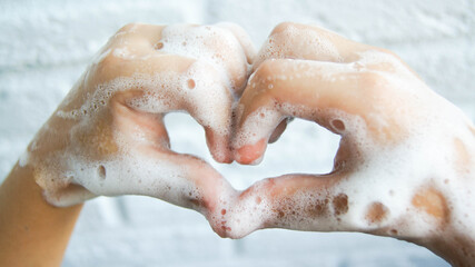 Washing hands with soap and foam. Heart-shaped fingers. Coronavirus pandemic protection by washing...