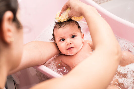 Mother cleaning 2 months baby in little bathtub