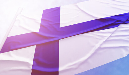 Finland flag on the blue sky. Close up national flag in bright rays sun that is waving in the wind on flagpole.