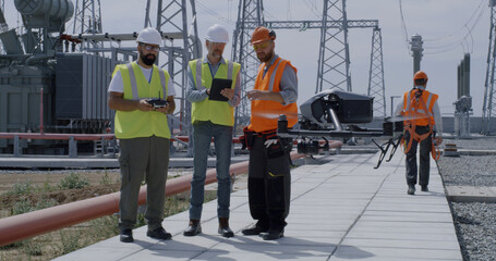 Employees using tablet and controlling drone on power station