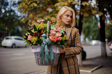 Fototapeta premium cute blonde woman holds wicker basket with various flowers and looks to the side