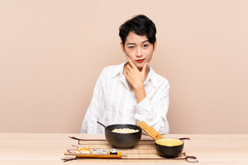 Young Asian girl in a table with bowl of noodles and sushi thinking an idea