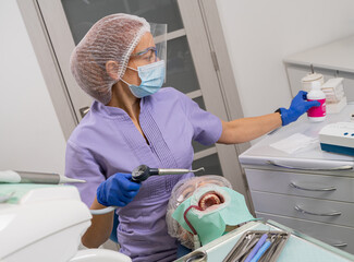 The dentist prepares the ultrasound machine, with his left hand takes a container with powder for cleaning teeth.