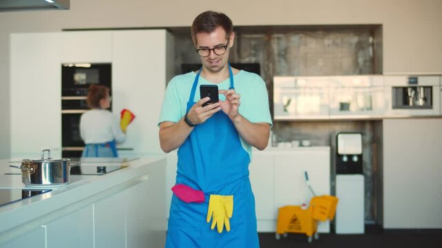 Male professional cleaner using smartphone standing in modern home kitchen
