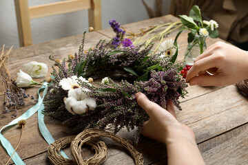 Florist making beautiful autumnal wreath with heather flowers at wooden table, closeup © New Africa