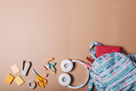 School supplies flat lay on craft paper background. Blue backpack, white headphones, notebook and pens with copy space.