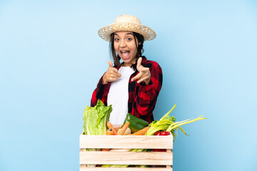 Young farmer Woman holding fresh vegetables in a wooden basket pointing to the front and smiling