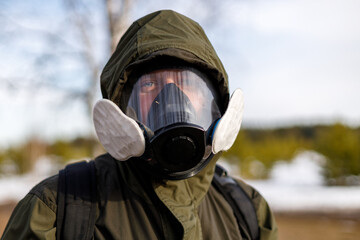 a man in a protective mask from gases looks into the frame against the background of nature