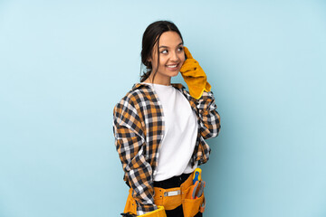 Young electrician woman isolated on blue background keeping a conversation with the mobile phone with someone