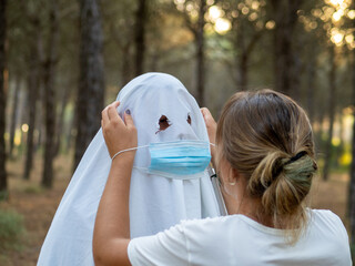 Closeup shot of a female putting a medical mask on a ghost costume-Halloween during COVID-19 concept