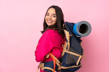 Young mountaineer girl with a big backpack over isolated pink background with arms crossed and looking forward