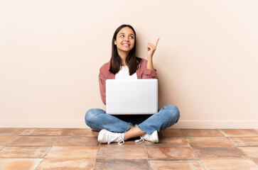 Young mixed race woman with a laptop sitting on the floor pointing up a great idea