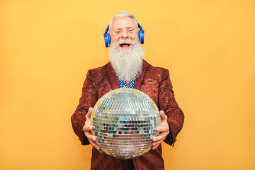 Crazy hipster man listening music with headphones while holding disco ball - Party concept