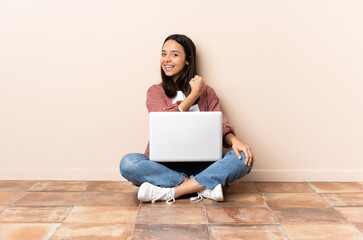 Young mixed race woman with a laptop sitting on the floor celebrating a victory