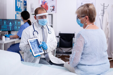 Obraz premium Discussing neck injury with female patient pointing tablet pc and wearing protective visor. Medical examination for infections, disease and diagnosis.